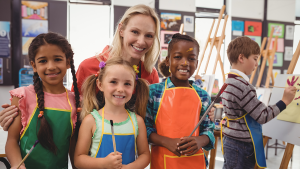 Art teacher standing behind four art students wearing paint smocks — art classrooms are underfunded